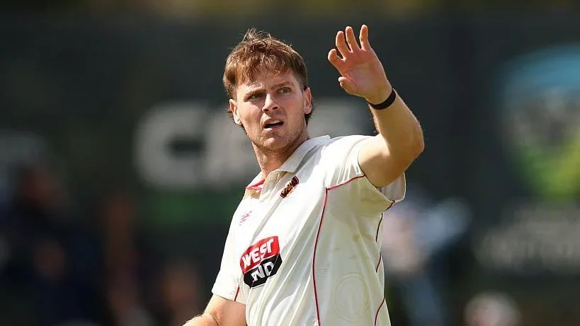 Liam Scott holding his left arm in the air to catch a ball that he is looking over his left shoulder towards. He is walking on the pitch during a match for Adelaide Strikers